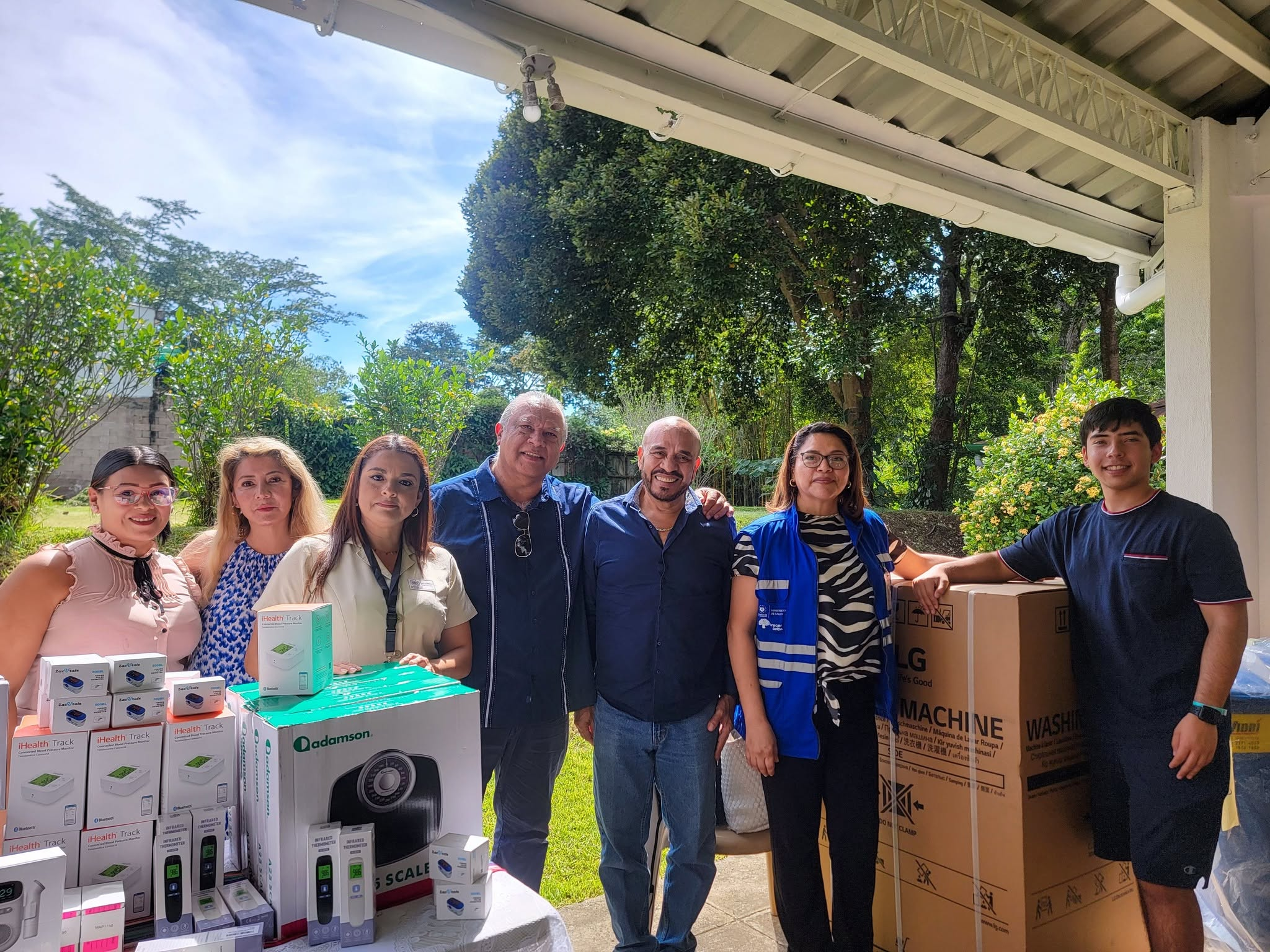 Standing with local and health representatives beside donated medical equipment and washing machines
